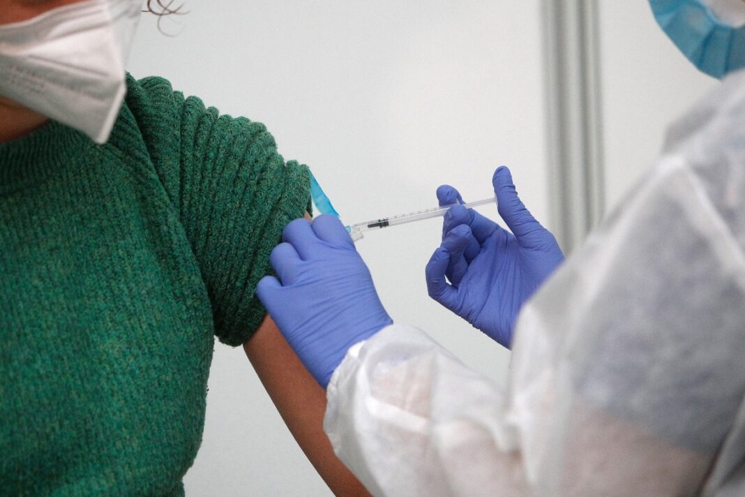 Una sanitària administra una dosi de la vacuna contra la Covid-19 a una dona amb mascareta
